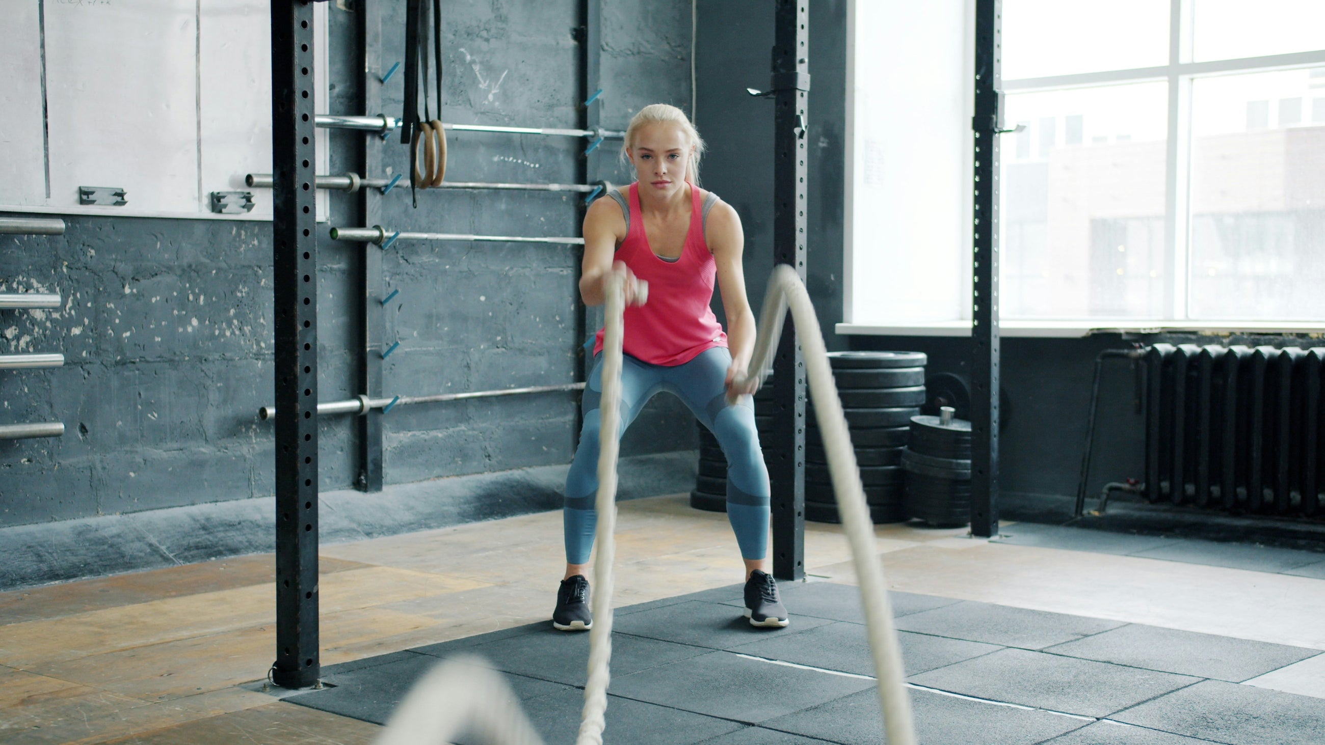 Woman in a pink tank top doing battle rope exercises in a modern gym